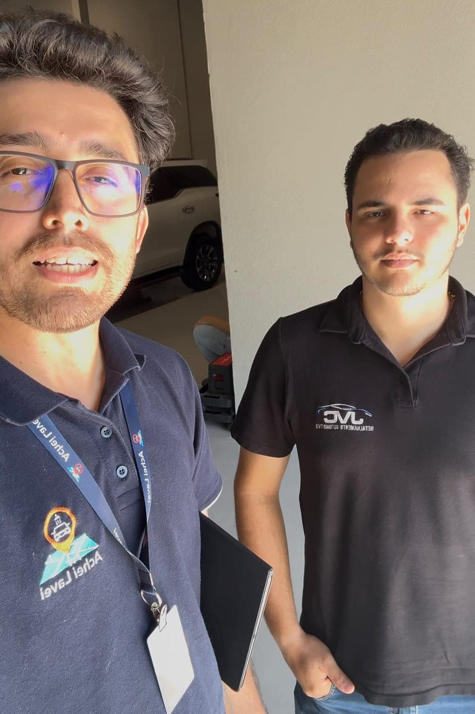 Integrante da equipe Achei Lavei ao lado de um profissional da JVC Detalhamento Automotivo, com um carro ao fundo